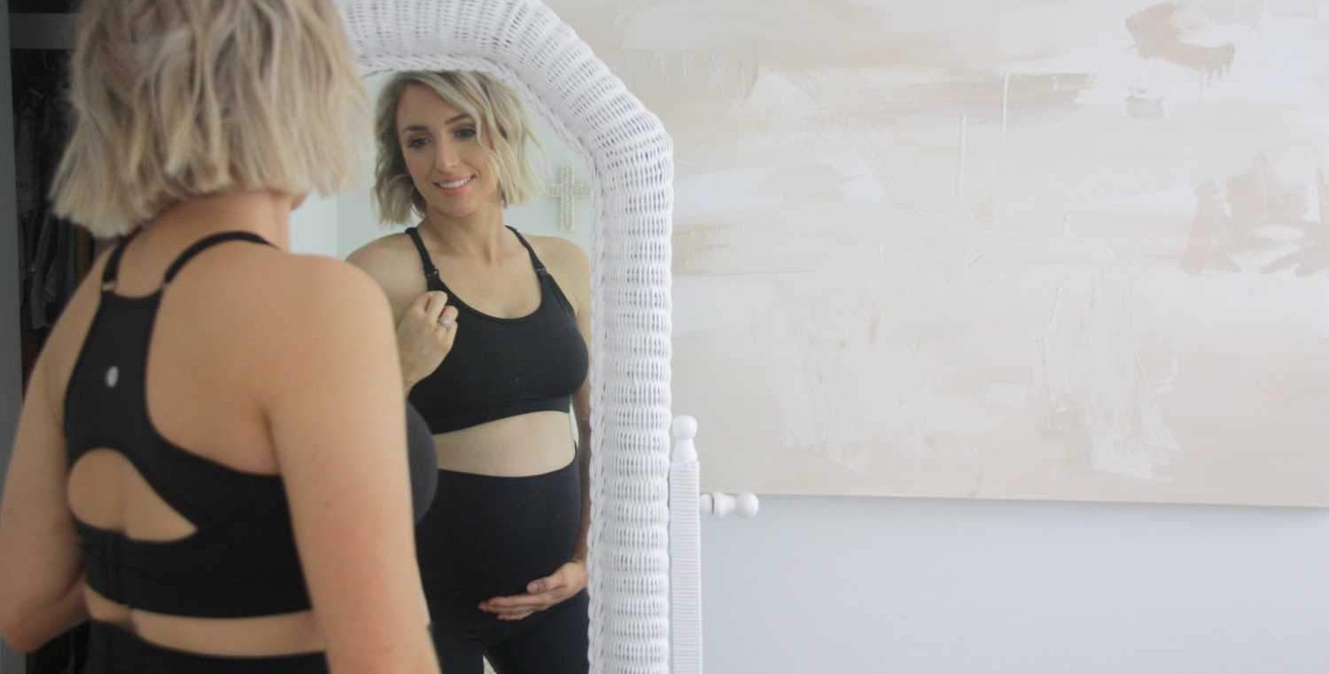 Woman in black maternity sports bra and black leggings looking in the mirror